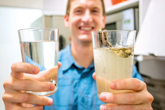 a man holds out a glass of clear water in one hand and a glass of cloudy polluted water in the other