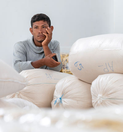 a man leans against large white bags of processed farinha