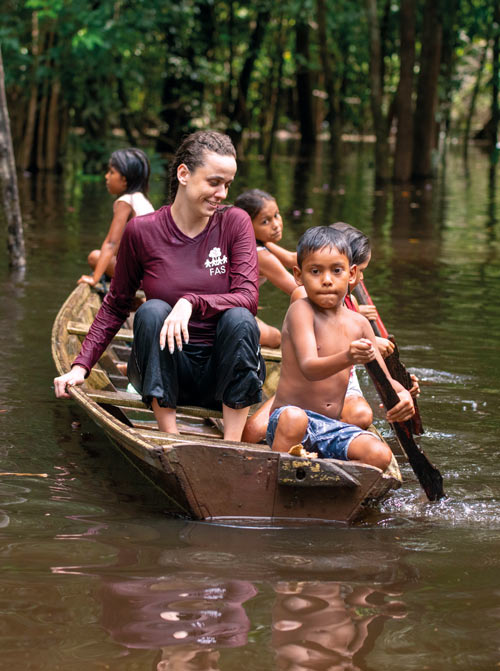 children guide a canoe on the river in the amazon with a young woman passenger