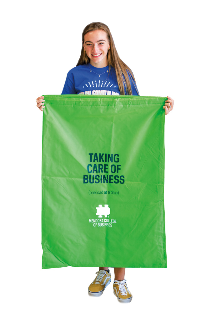 a student holds up a large green canvas laundry bag that says taking care of business one load at a time