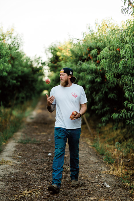 a man walks through a fruit grove tossing peaches in the air