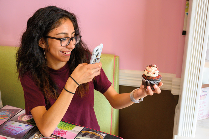 a student takes a photo of a fancy cupcake with her cell phone
