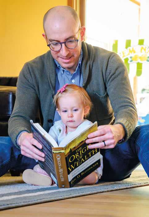 Jason Reed and baby looking at book about the origin of wealth