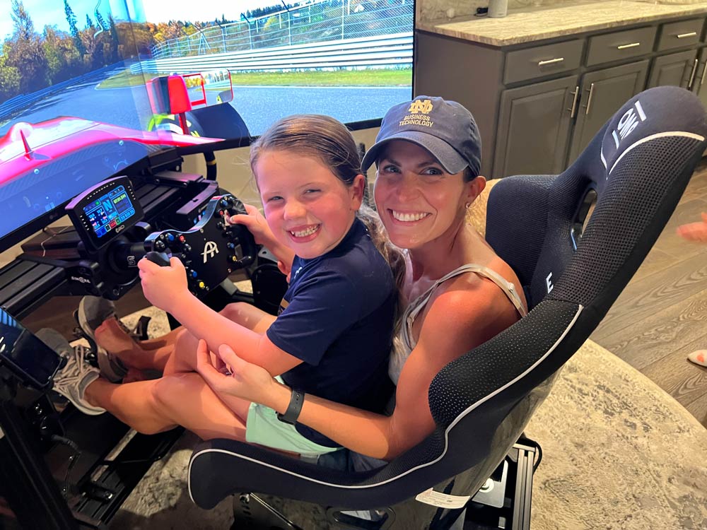 (Katie and one of her children playing on the racing game her husband Adam built in their basement)